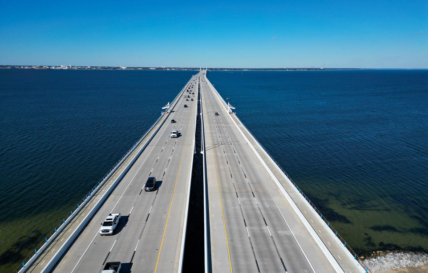 Aerial view of the Pensacola Bay Bridge running straight across deep blue water toward the city shoreline.