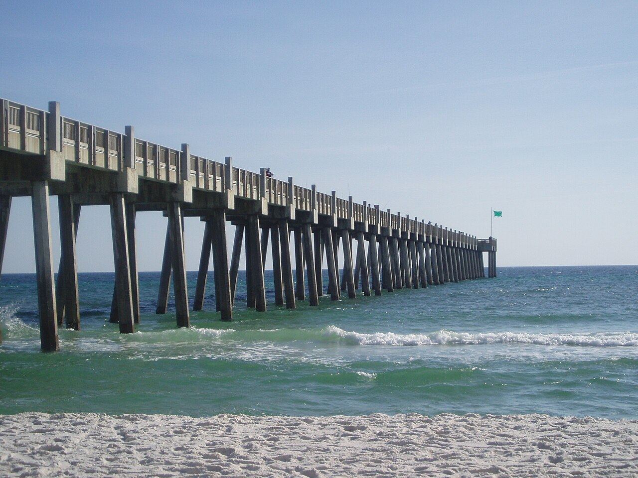 Emerald Gulf water and white sand beside the long concrete Gulf Pier at Pensacola Beach.
