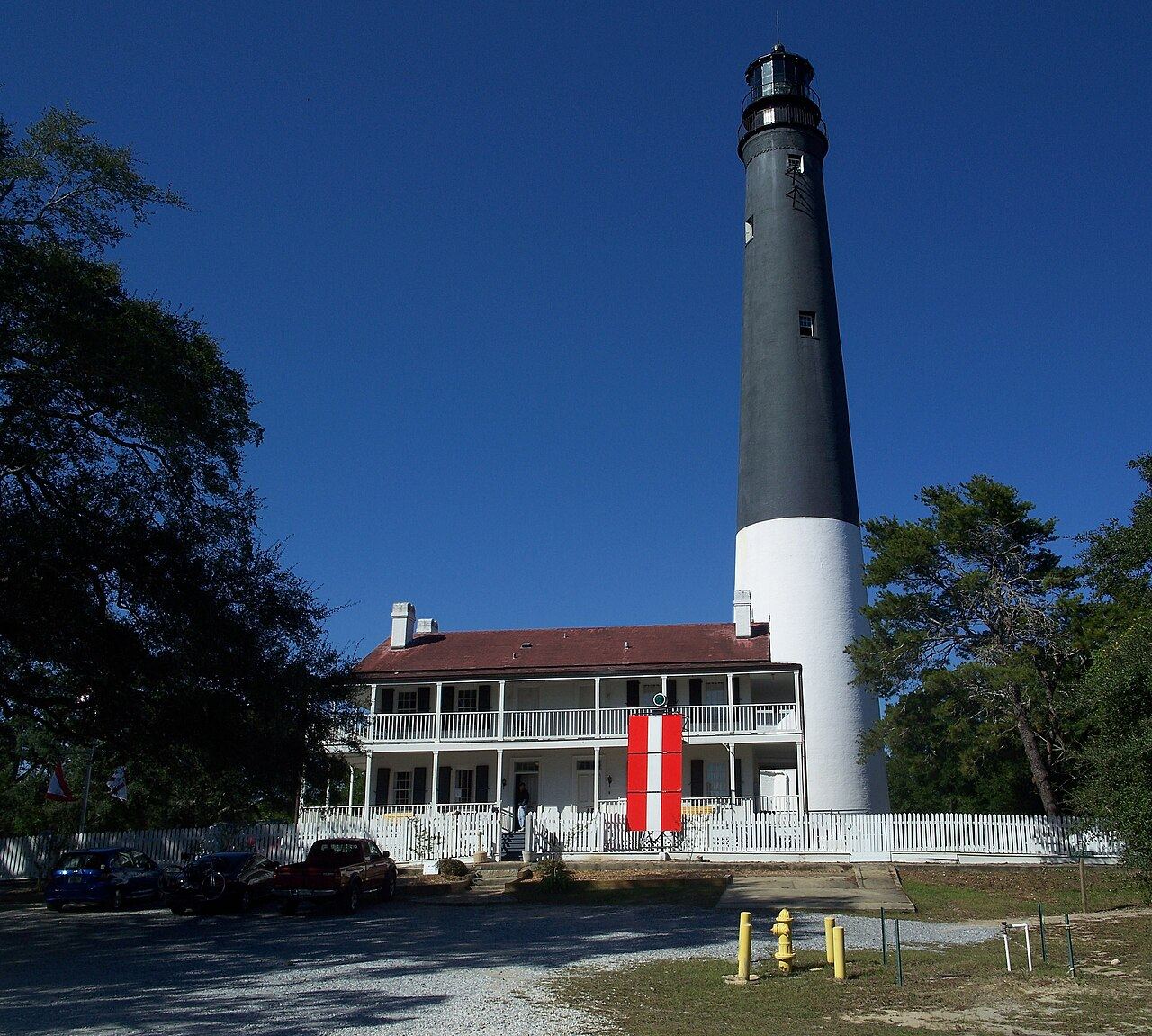 The black-and-white Pensacola Lighthouse rising behind the keeper's quarters under a deep blue sky.