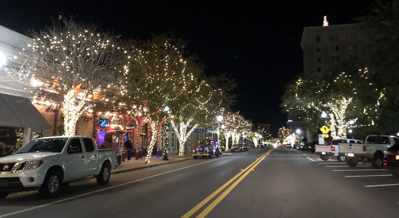Palafox Street downtown at night, its trees wrapped in white string lights above parked cars.